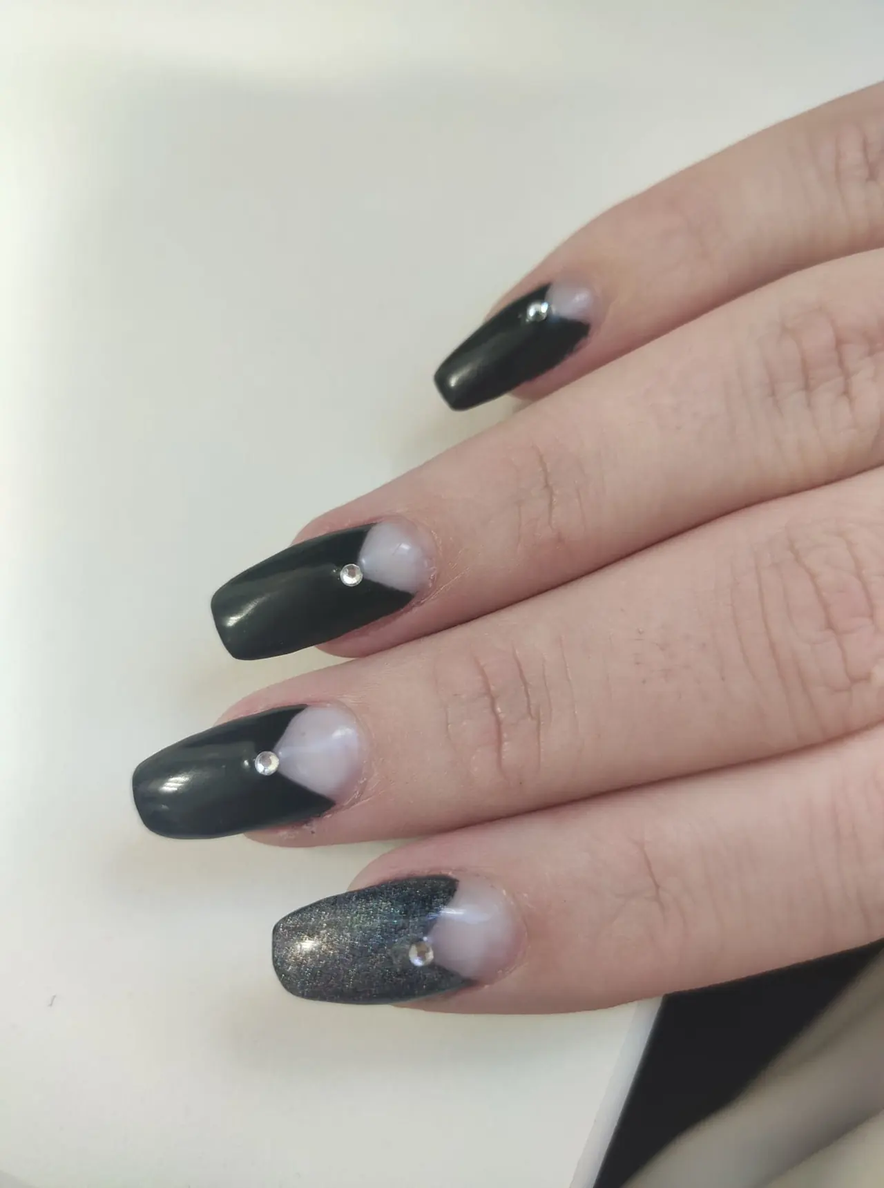 Glossy black square nails with pale half-moon cuticles and small rhinestone accents