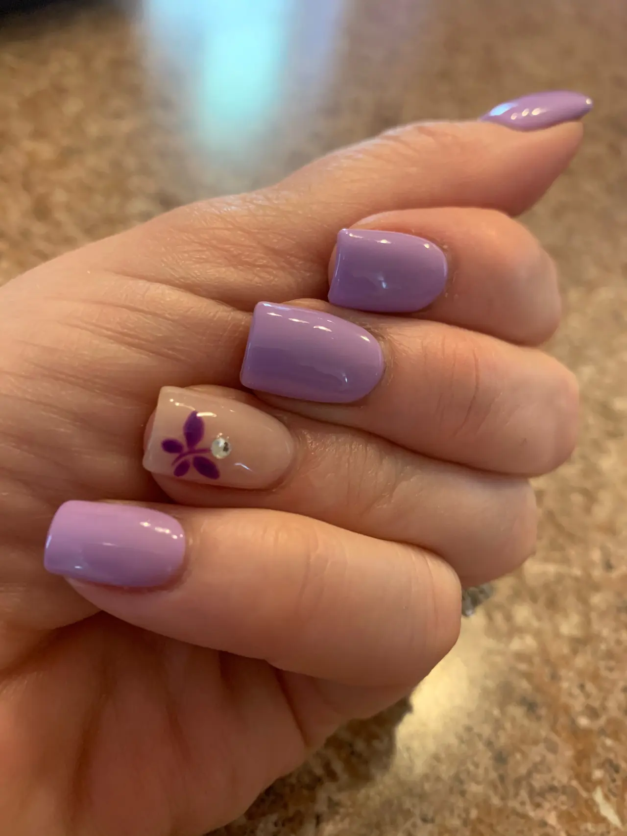 Lavender acrylic nails with a nude flower accent and small crystal detail