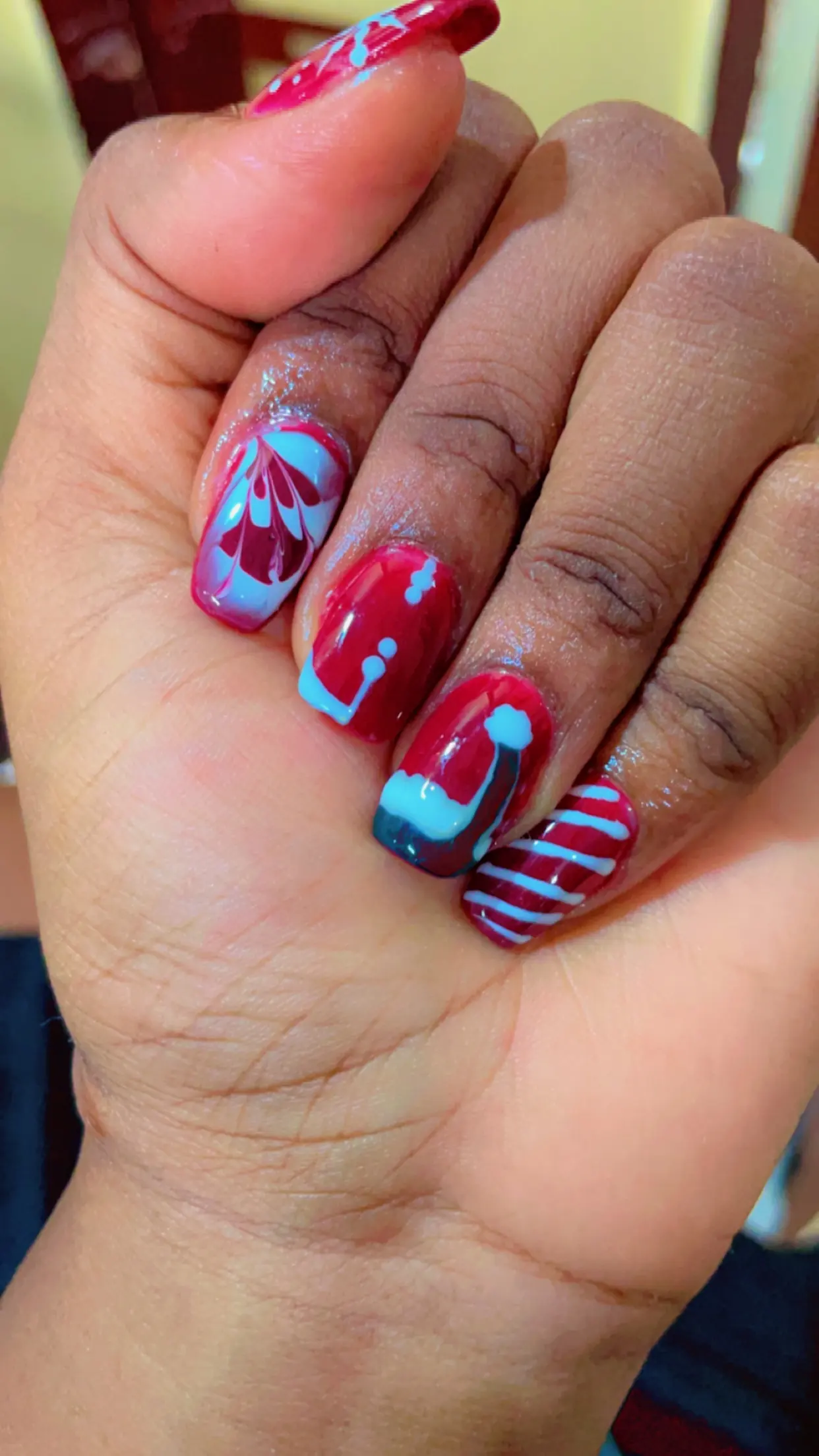 Red acrylic nails with blue abstract accents and a glossy gel finish