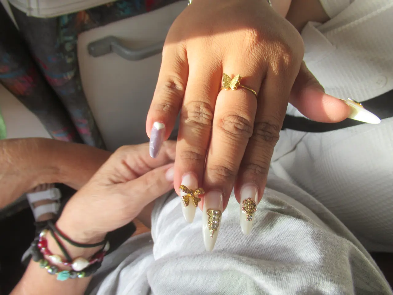 Long white stiletto nails with gold 3D bow charms and raised gold details